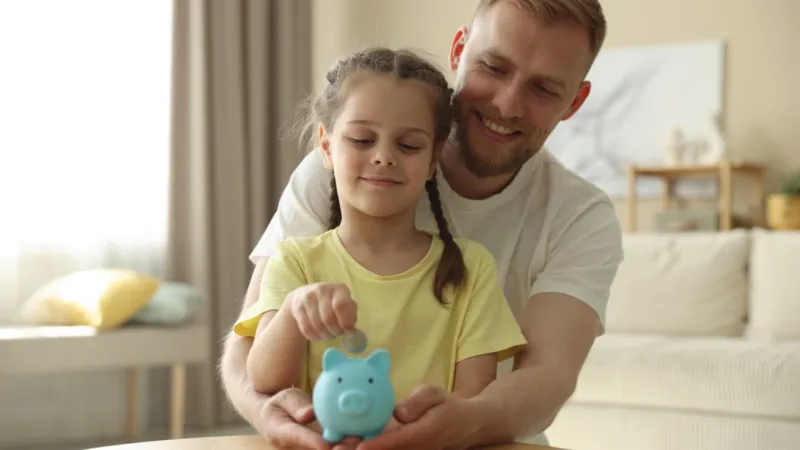 Ein Papa legt zusammen mit der Tochter Geld ins Sparschwein